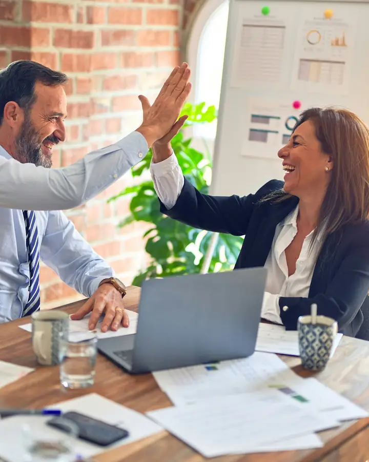 Twee collega's geven elkaar een high five aan hun bureau