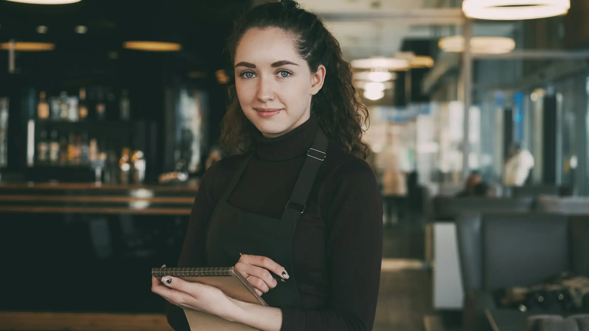 Een serveerster met een tablet staat lachend in een restaurant