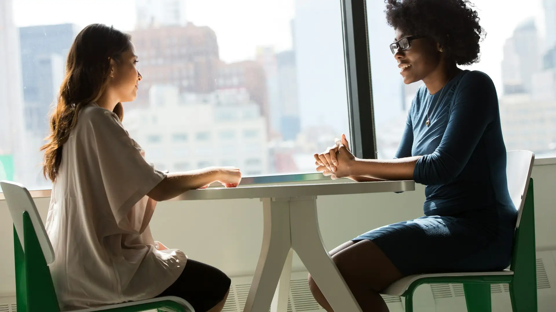 Twee vrouwen in gesprek aan een tafel bij het raam